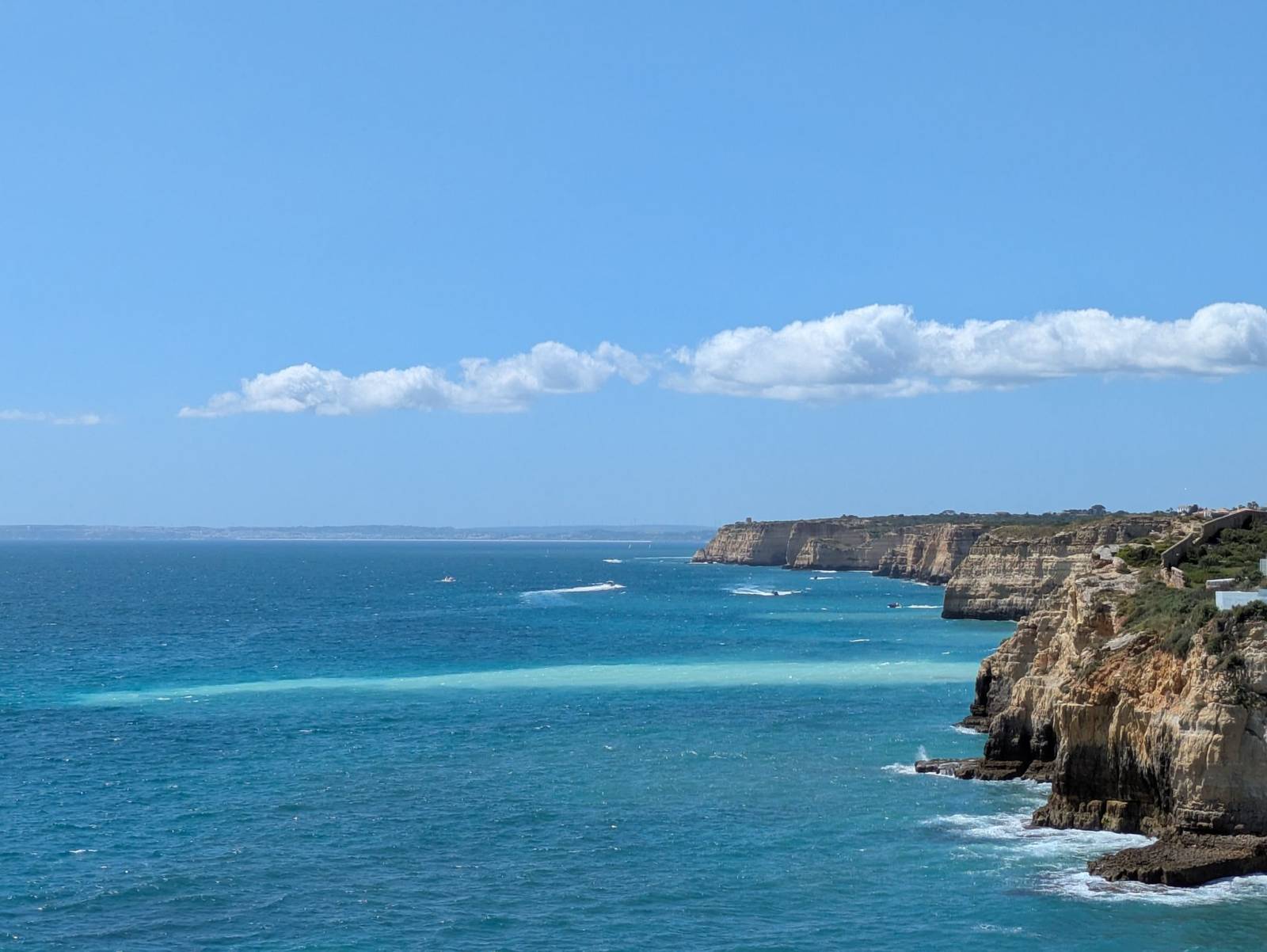 Sunlit cliffs and clear blue sea along the Algarve coastline in the Faro district of Portugal